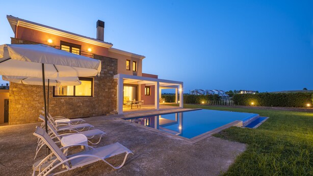 A modern house with a swimming pool, outdoor seating, and a well-lit patio area.