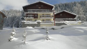 A multi-story building with balconies, surrounded by snow-covered trees and a clear sky.