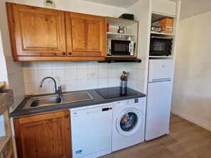 A compact kitchen with wooden cabinets, a built-in microwave, a dishwasher, and a washing machine.