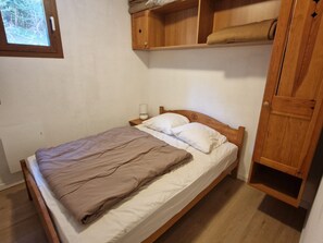 A single bed with a wooden headboard, a bedside table with a lamp, and a wooden wardrobe with a towel hanging on it. - 3BR+Cabin Apt, 8 ppl, near ski lifts, parking (Valfréjus)