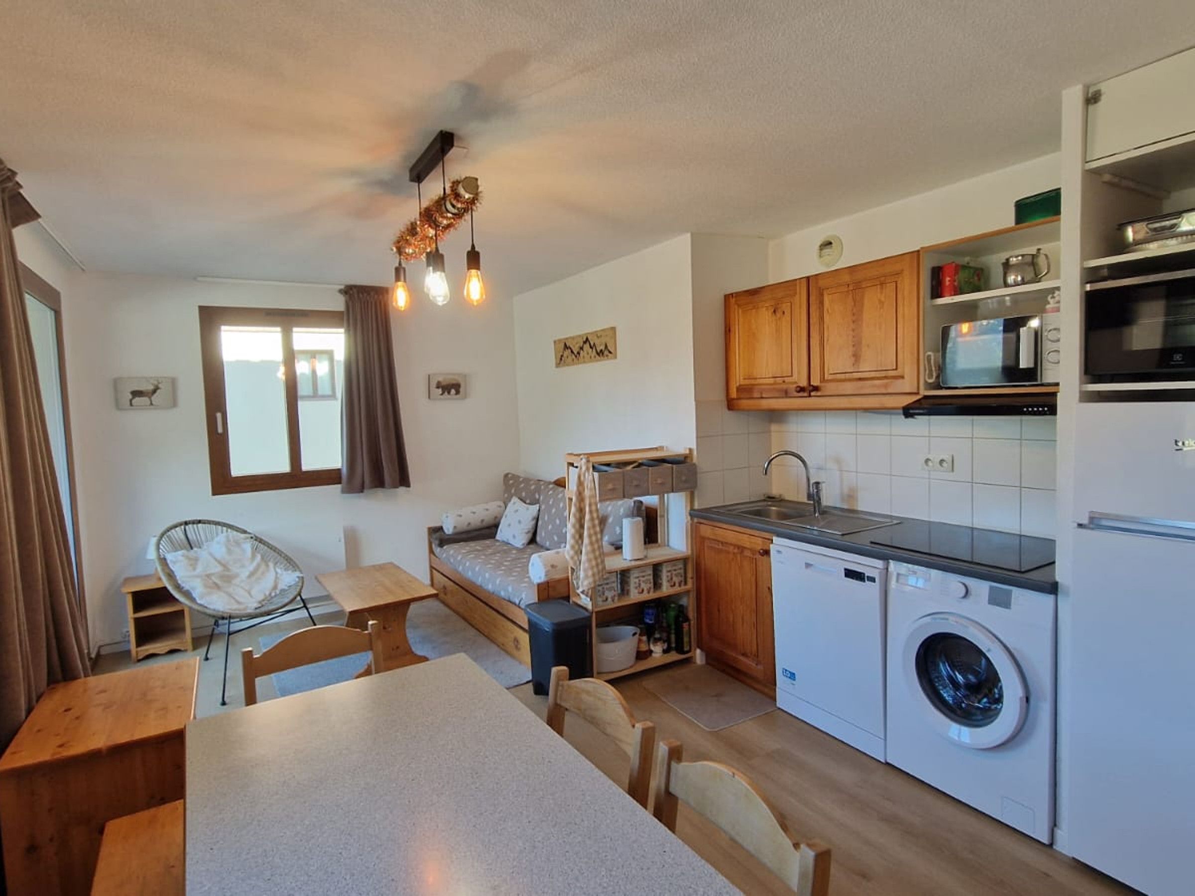 A compact kitchen with a washing machine, wooden cabinets, and a dining area with a table and chairs.