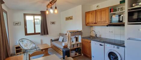 A compact kitchen with a washing machine, wooden cabinets, and a dining area with a table and chairs.