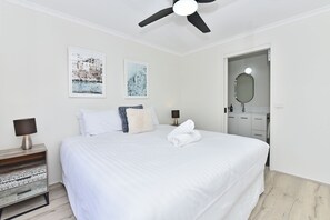 Een hotelkamer met een bed, nachtkastje, lamp, plafondventilator en twee ingelijste foto's aan de muur.