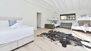 Un dormitorio moderno con una cama grande, una cama más pequeña, un sofá y una alfombra de cuero de vaca.