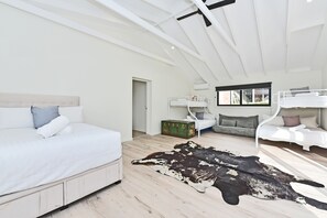 Un dormitorio moderno con una cama grande, una cama más pequeña, un sofá y una alfombra de cuero de vaca.