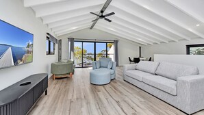 Un amplio salón con techo alto, un ventanal con vista al mar y muebles modernos.