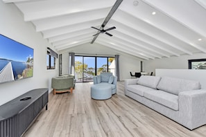 Un amplio salón con techo alto, un ventanal con vista al mar y muebles modernos.