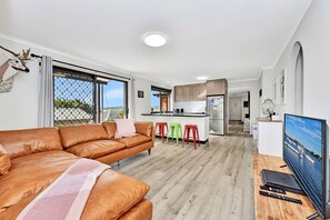 Een moderne woonkamer met een leren bank, een televisie en een keuken op de achtergrond.
