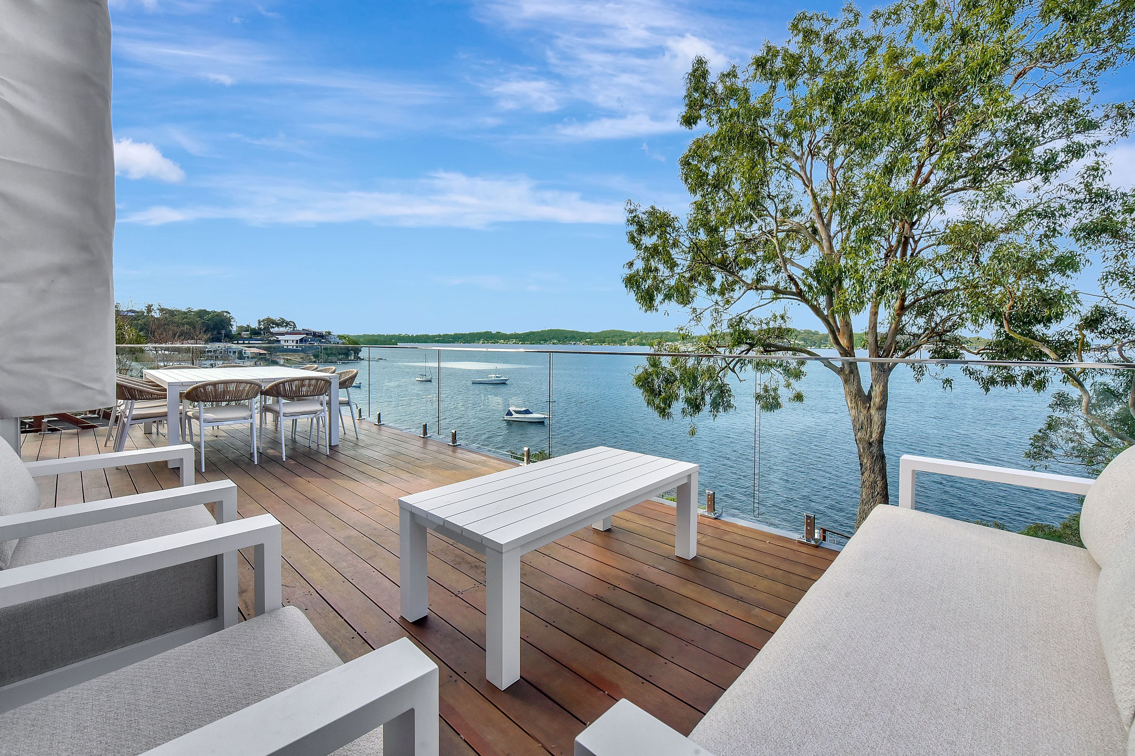 A deck with white furniture overlooking a calm body of water with boats.