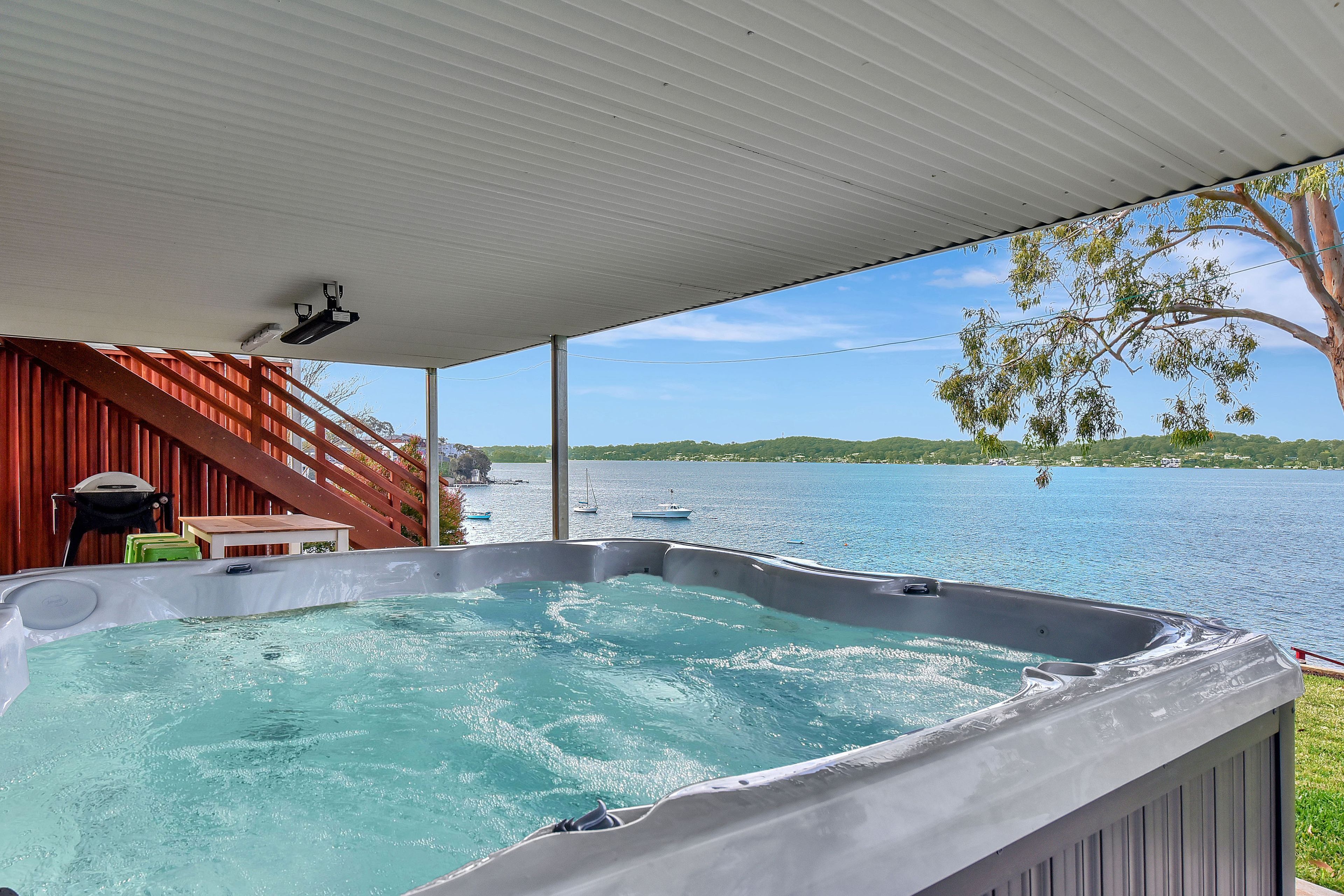 A hot tub under a covered area with a view of a lake and boats.