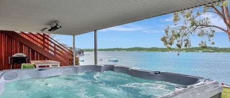 A hot tub under a covered area with a view of a lake and boats.