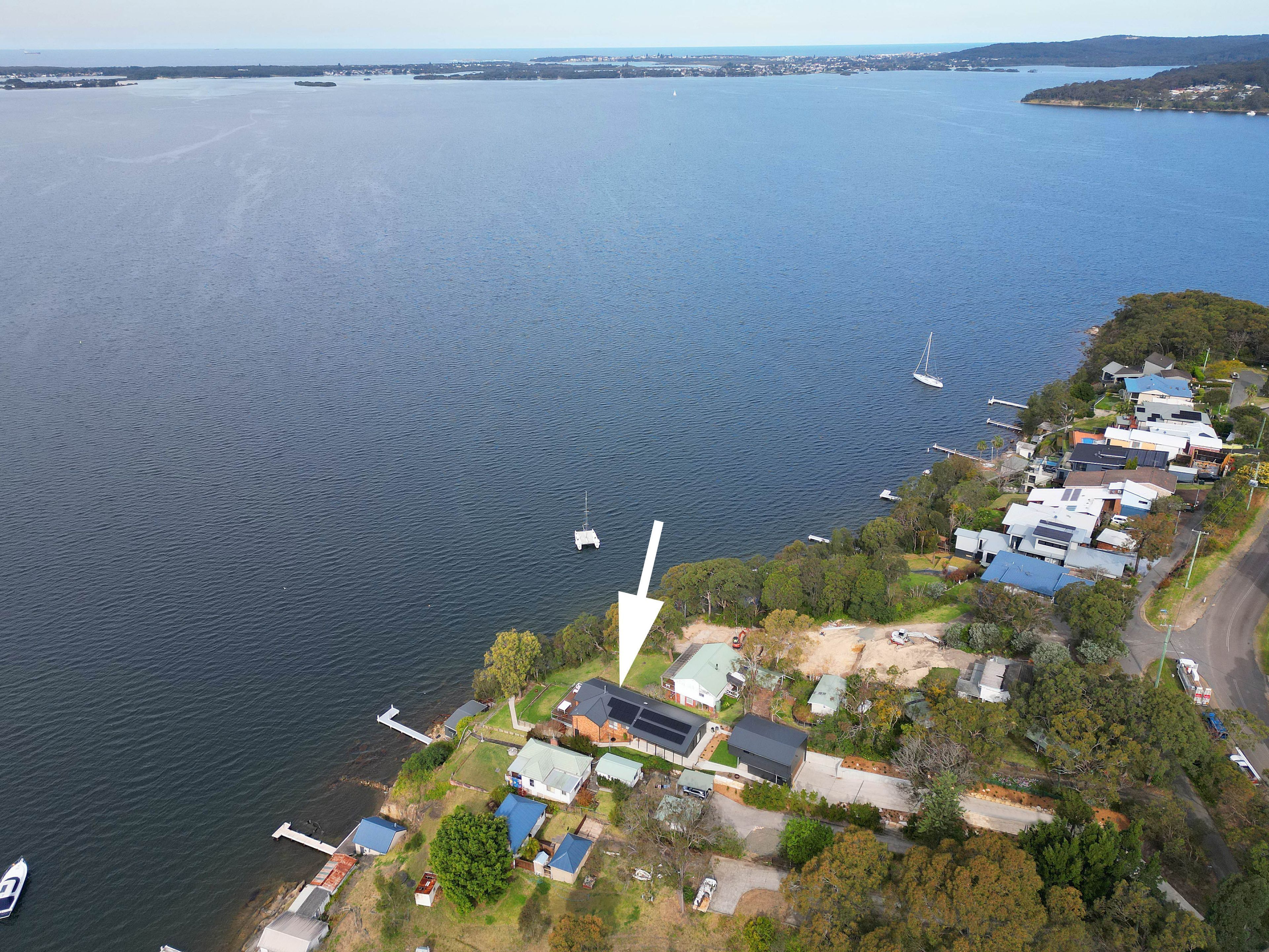 An aerial view of a coastal residential area with houses, a dock, and a body of water.