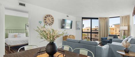 Une chambre d’hôtel moderne avec une table à manger en bois, un canapé, une télévision et un balcon offrant une vue agréable.