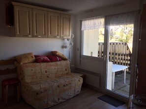 Une pièce avec un canapé, une fenêtre donnant sur une terrasse et une porte menant à l’extérieur.