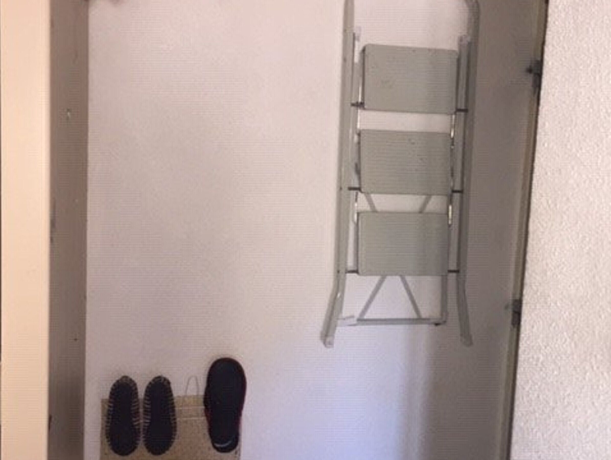 Um corredor com um par de sapatos pretos no chão, uma parede branca e um suporte de metal para cadeiras encostado na parede.