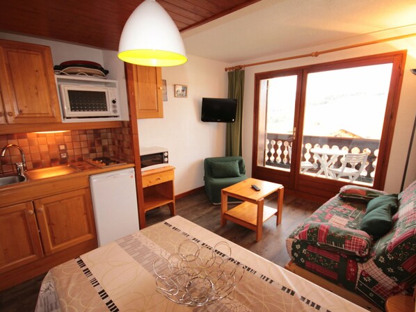 A compact living space with a kitchenette, a dining area, a sofa, and a balcony with a view.