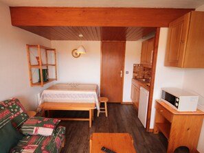 A compact room with a bed, a small kitchenette, a wooden ceiling, and a green sofa.