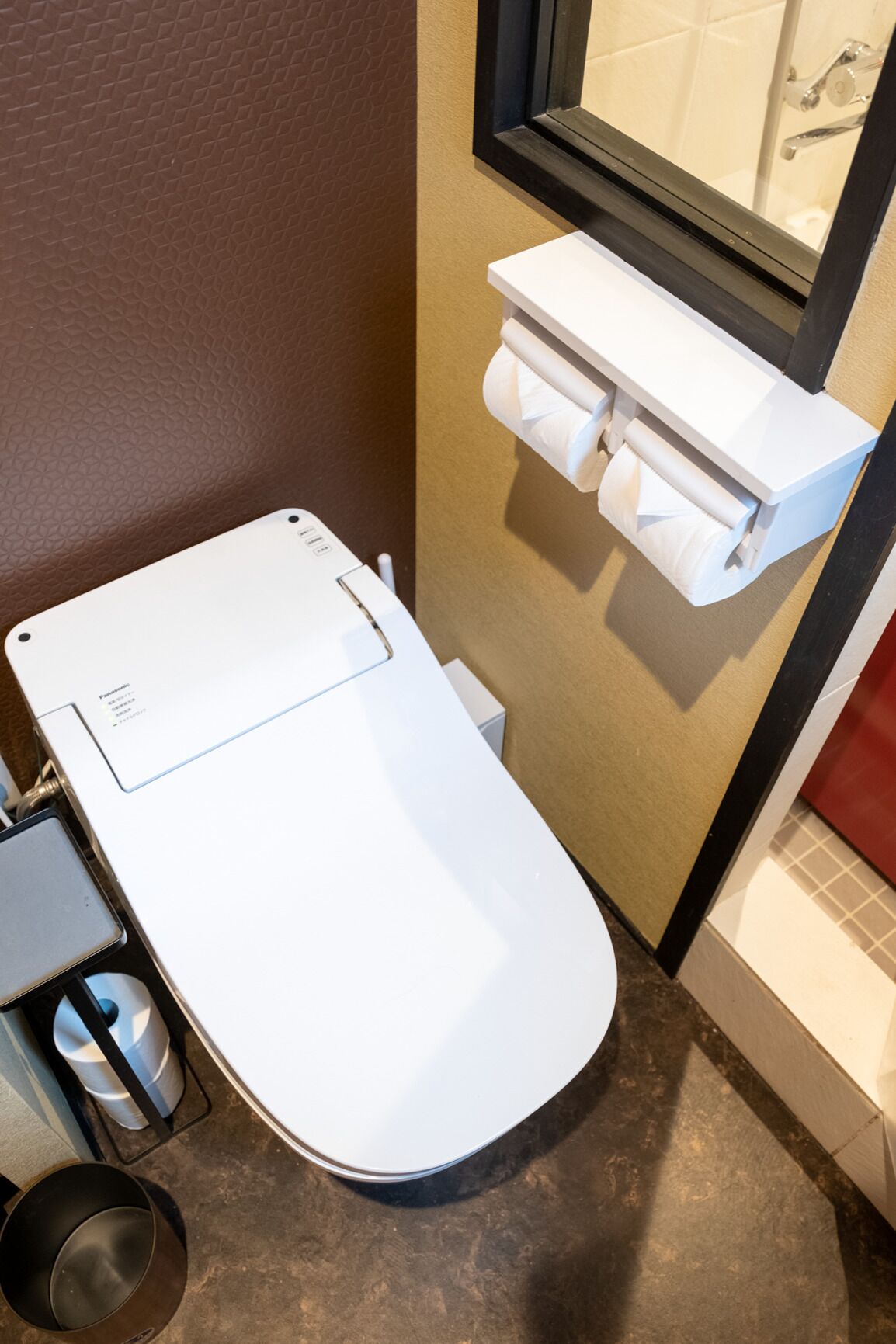 Un baño pequeño con inodoro blanco, un estante con papel higiénico y una zona de ducha visible.