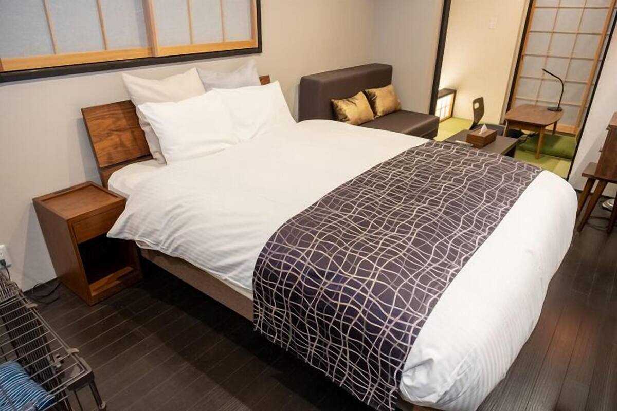 Un lit bien fait, recouvert d’une couvre-lit à motifs, une table de chevet, une chaise et un petit bureau avec une lampe.