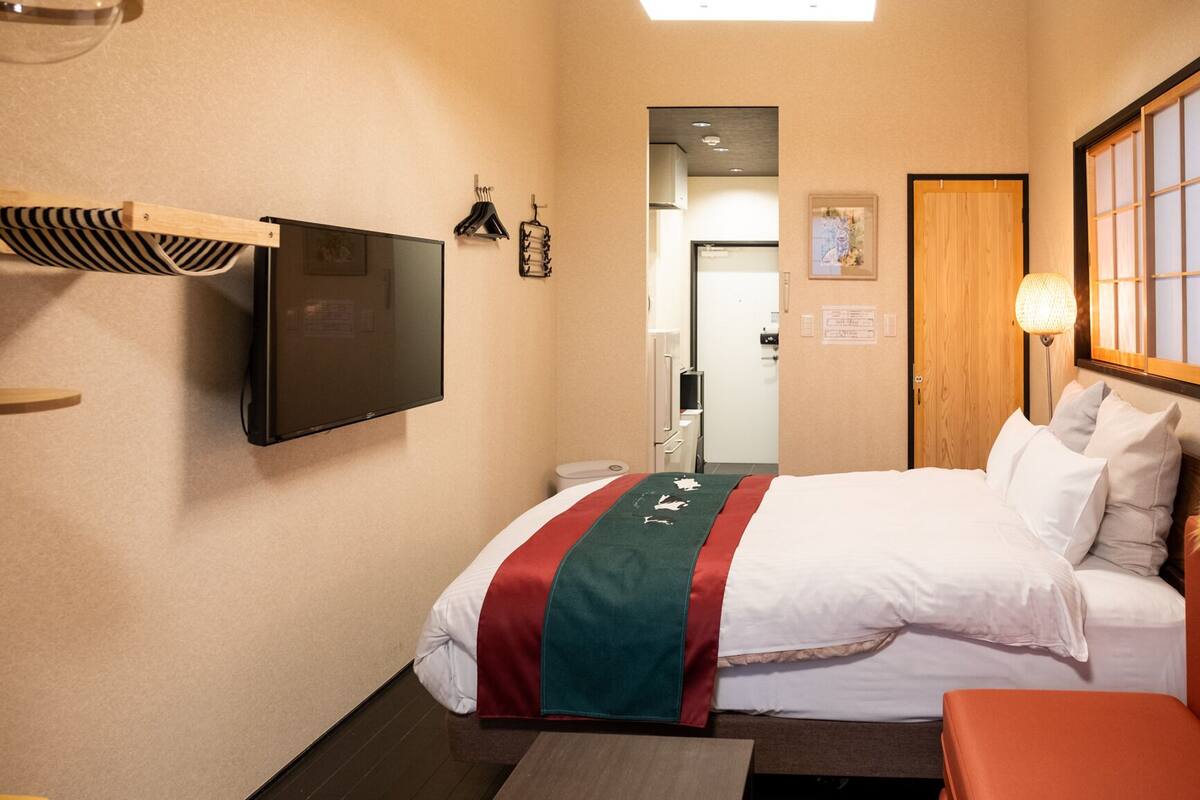 Une chambre d’hôtel avec un lit, un téléviseur fixé au mur, une table de chevet, une lampe et une porte en bois.