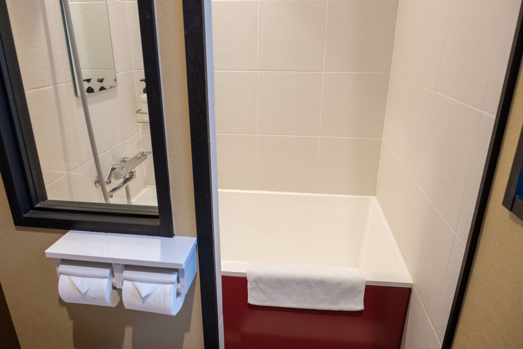 Un baño con una bañera blanca, un espejo y un perchero con toallas.