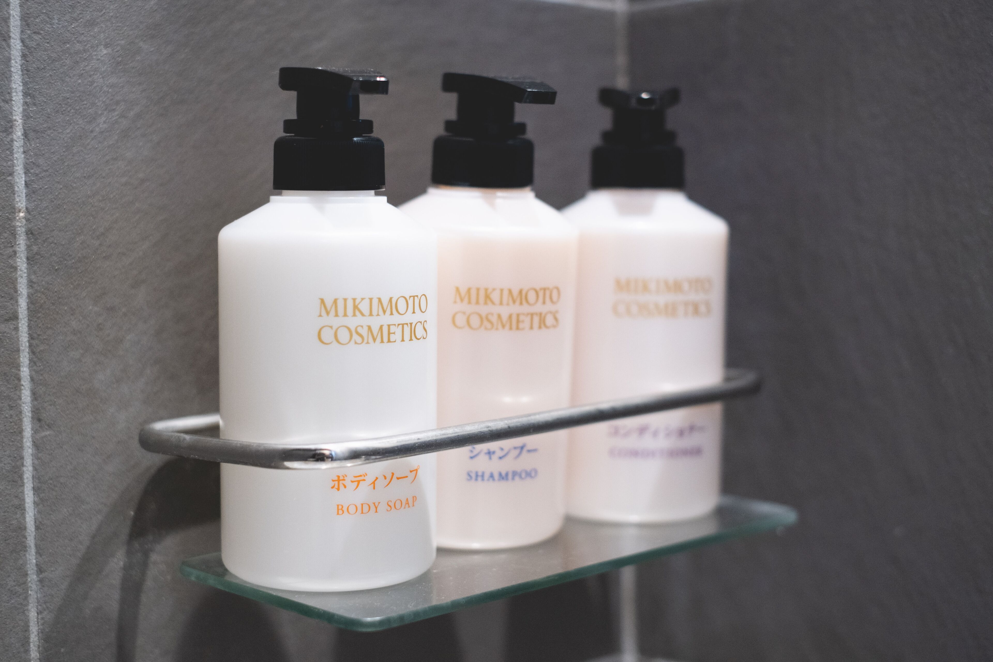 Three bottles of MIKIMOTO COSMETICS on a glass shelf in a bathroom.