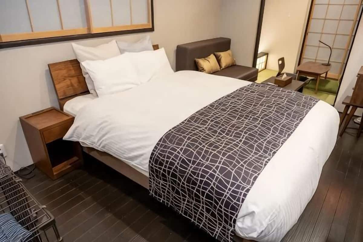 Un lit bien fait, recouvert d’une couvre-lit à motifs, une table de chevet avec une lampe et une chaise dans une chambre d’hôtel moderne.