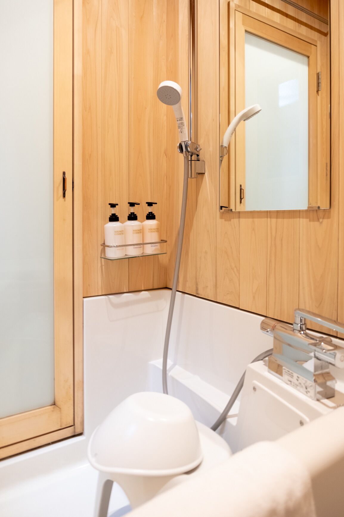 A modern bathroom with a wooden vanity, a shower with a handheld showerhead, and a white bathtub.