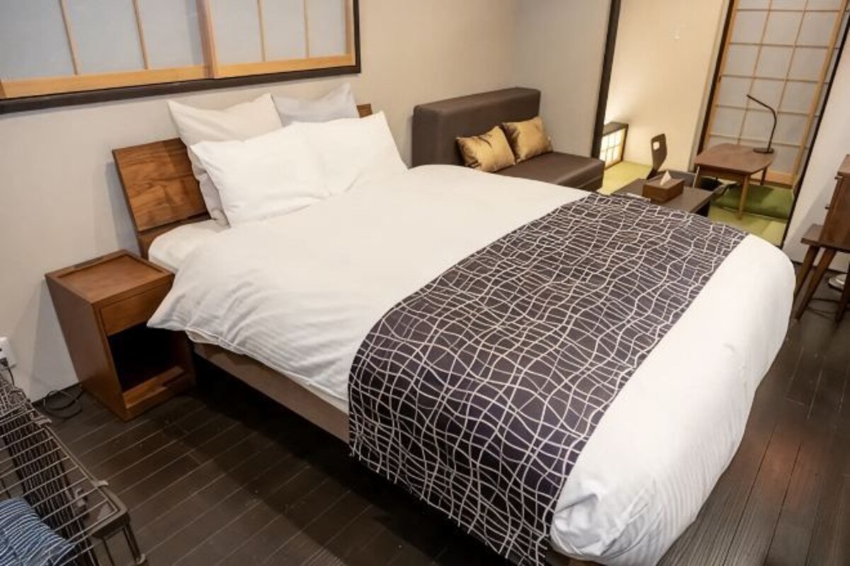 A neatly made bed with a patterned bedspread, a bedside table with a lamp, and a chair in a modern hotel room.