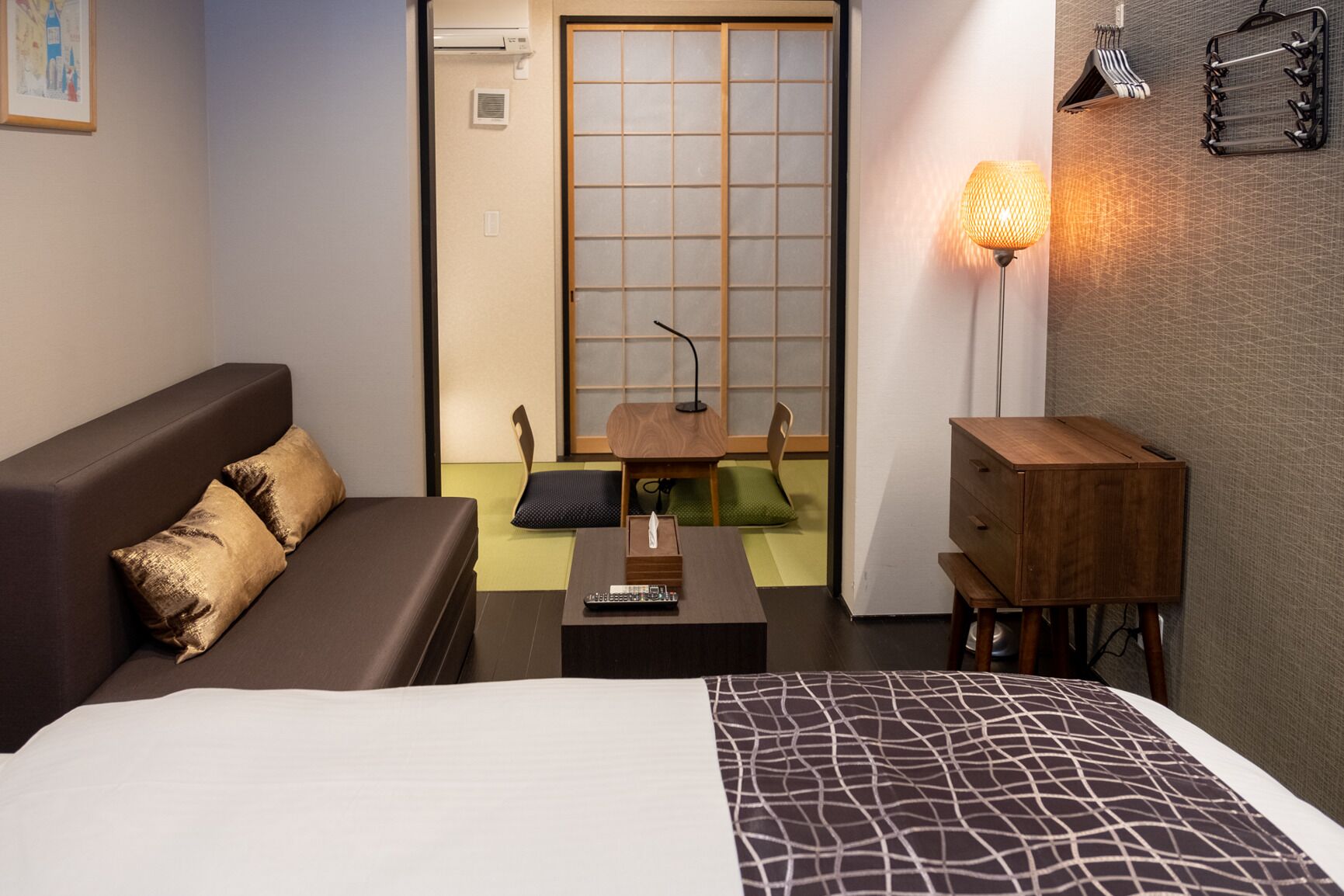 A hotel room with a bed, a sofa, a small table, a lamp, and a wooden cabinet.