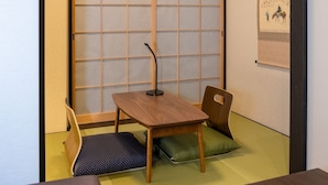 A traditional Japanese room with tatami flooring, a sliding shoji screen, a wooden table with a microphone, and a green cushion.