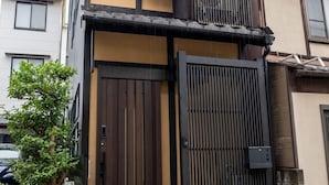 A two-story building with a traditional Japanese architectural style, featuring a wooden gate and a small wooden bench outside.