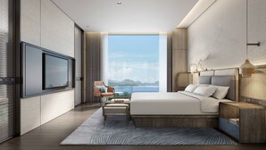 A modern bedroom with a large bed, a TV mounted on the wall, a view of the sea, and a small seating area. - Courtyard by Marriott Liuzhou Sanjiang (Liuzhou)