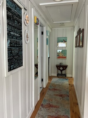 A hallway with a chalkboard with rules, a wooden floor, and a painting on the wall.