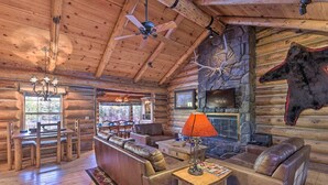 L’intérieur d’une cabane en rondins, avec une cheminée en pierre, des fauteuils en cuir, un bar en bois et un ventilateur de plafond.