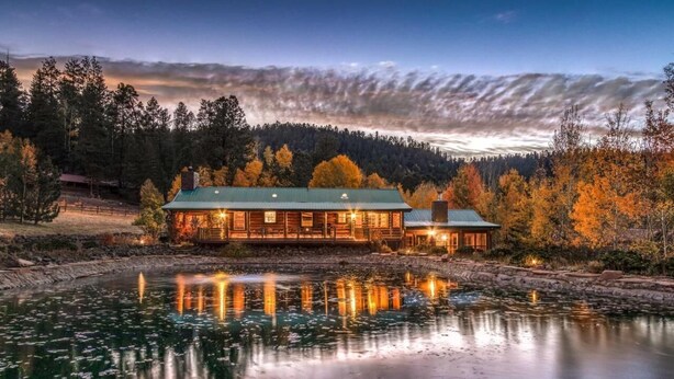 Un chalet doté d’un toit végétalisé, situé au bord d’un lac aux eaux calmes, et entouré d’arbres aux couleurs automnales.