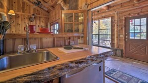 A rustic wooden interior with a wooden ceiling, a stone fireplace, and a large window with a view of trees. - Greer Lodge- Guest Quarters (Greer)