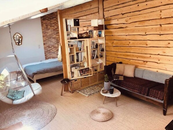 A cozy room with a loft bed, a wooden bookshelf, a sofa, and a hanging chair.