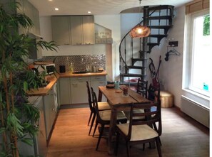 A modern kitchen with a wooden dining table, chairs, and a spiral staircase.