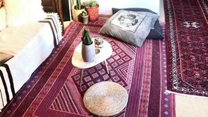Een gezellige kamer met een bed, een klein tafeltje met planten, een spiegel en een vloerkleed.