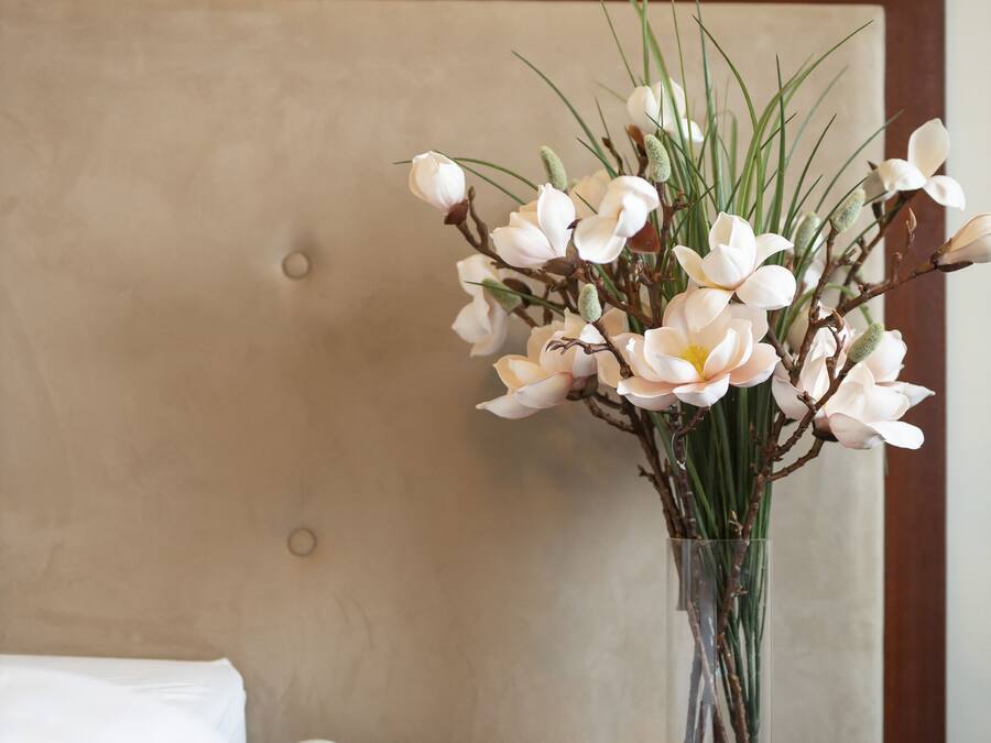 Ett hotellrum med en säng, ett sängbord, en telefon och en vas med blommor.