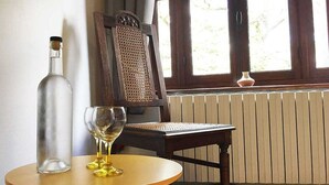Una habitación con una mesa redonda de madera, una botella y dos copas de vino. Hay una silla con respaldo de mimbre y una ventana con vistas a la vegetación.