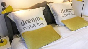 Una cama con dos almohadas que dicen "dreams come true" y una lámpara de noche.