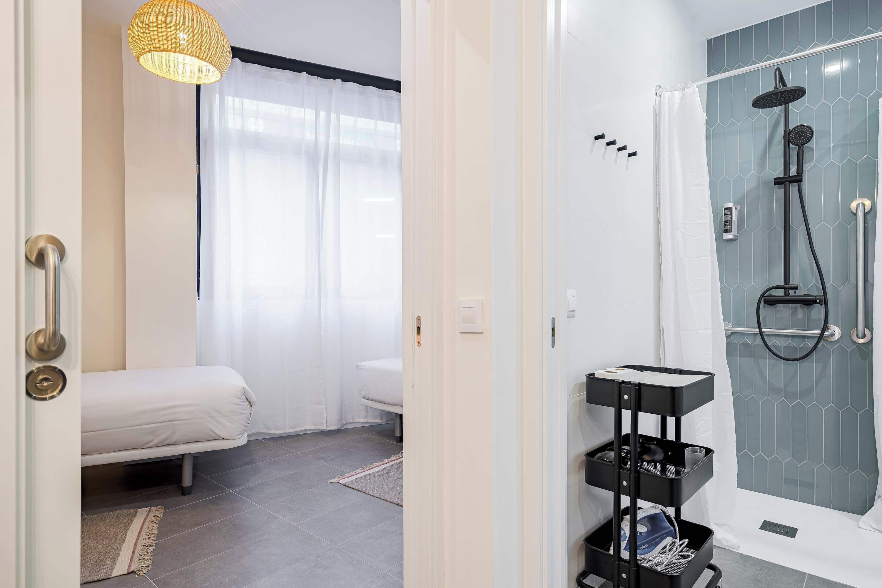 A modern bathroom with a shower, a toilet, and a bed in the adjacent room.