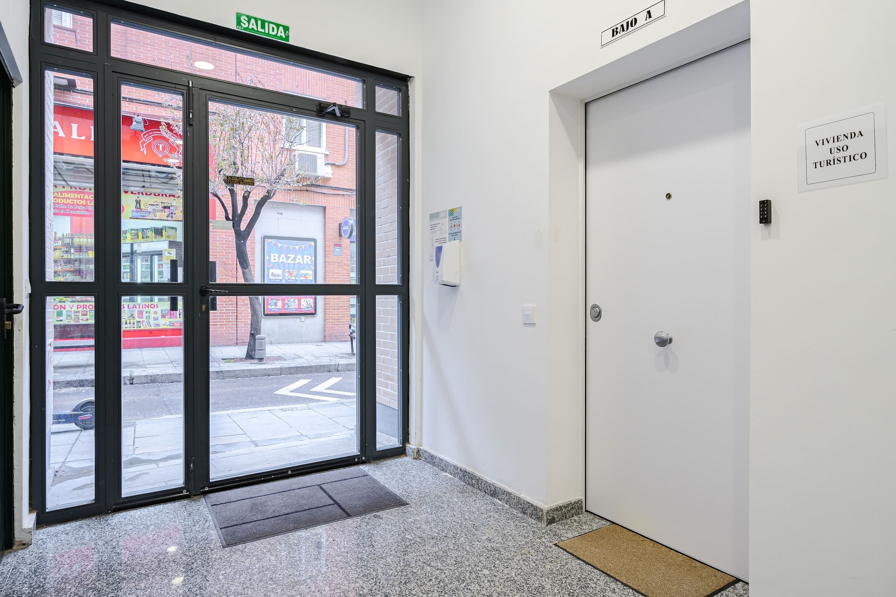 Entrada de hotel con puerta de cristal, un cartel que indica 'BAJO A' y un letrero que dice 'VIVIENDA USO TURÍSTICO'.