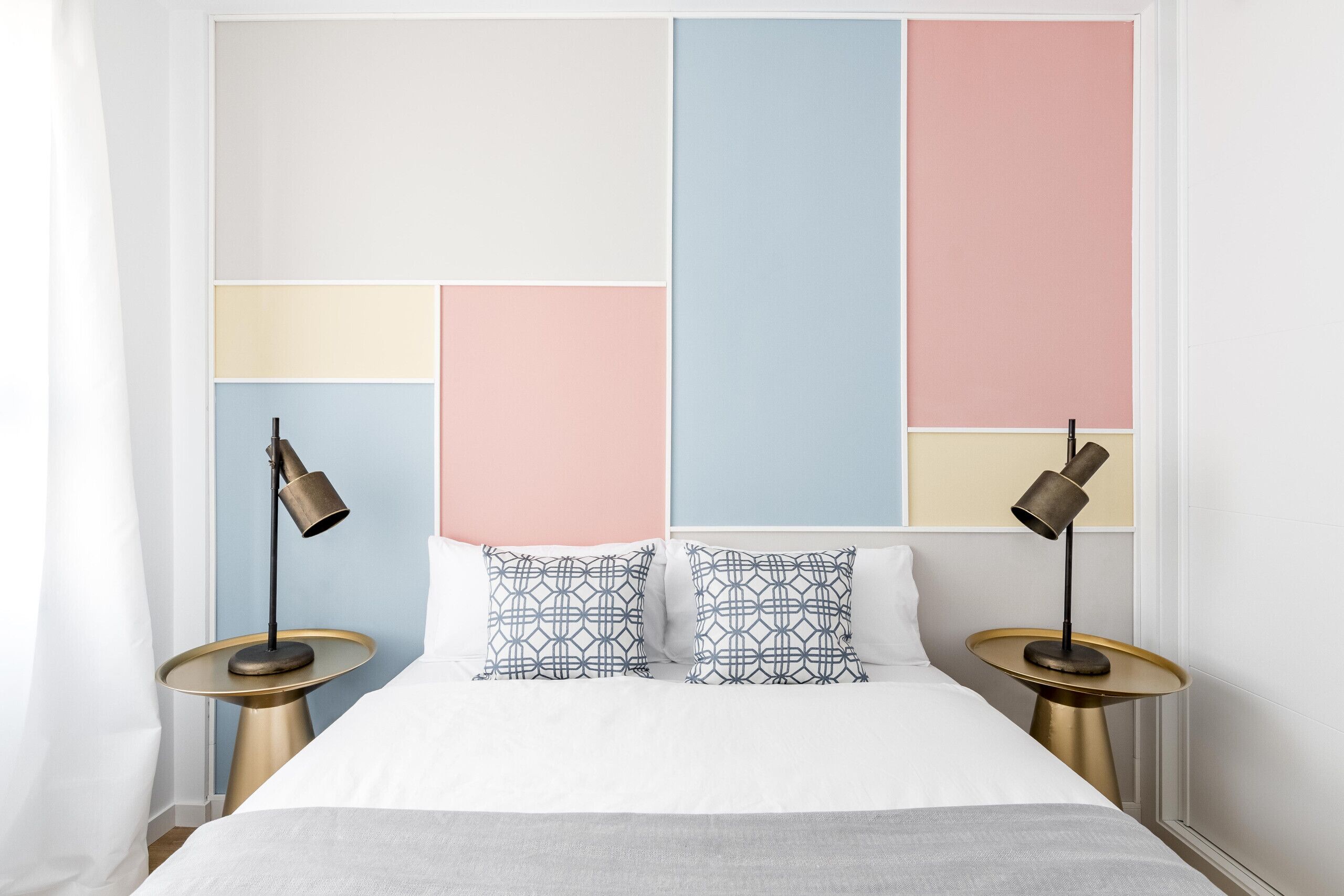 A neatly made bed with a white duvet, two patterned pillows, and two bedside lamps on gold bases.