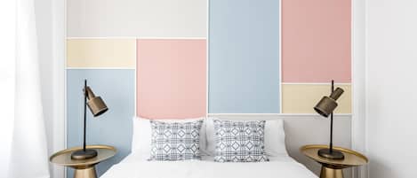 A neatly made bed with a white duvet, two patterned pillows, and two bedside lamps on gold bases.