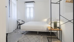 A minimalist bedroom with a bed, a chair, a desk, and a hanging light fixture.