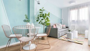 A modern living room with a light blue wall, a grey sofa, a coffee table, and a dining area with wireframe chairs.