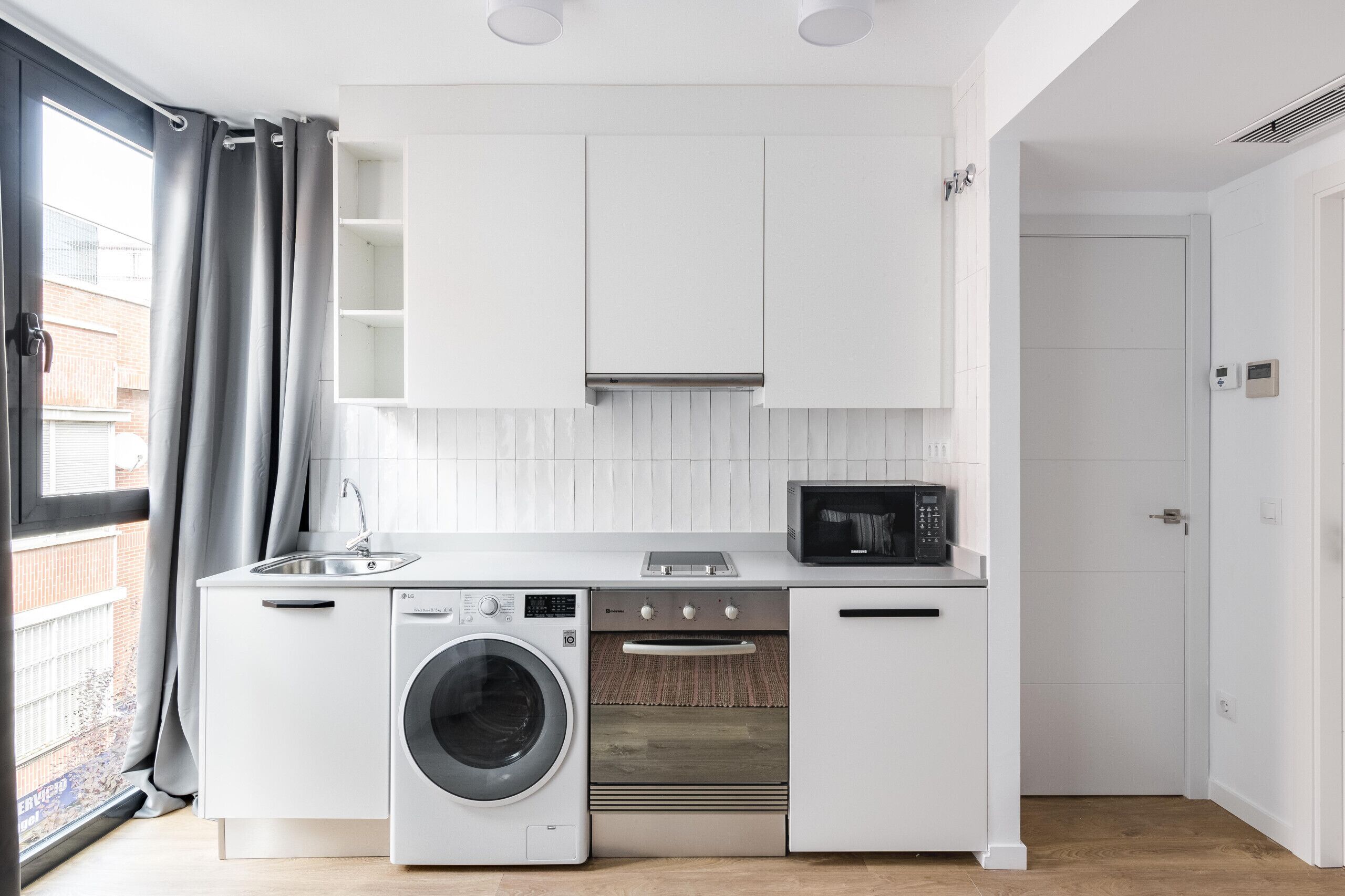 Une cuisine compacte équipée d’un lave-linge, d’un four à micro-ondes et d’un four traditionnel.